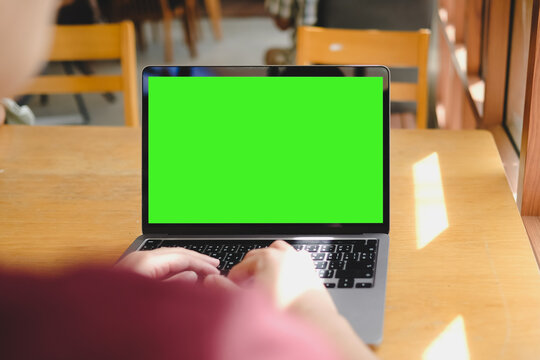 Close-up of hands typing on laptop computer keyboard with green screen display mockup for chroma key replacement