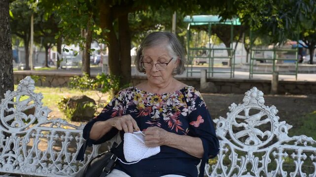 Older Woman Knitting on a Bench in a Public Park