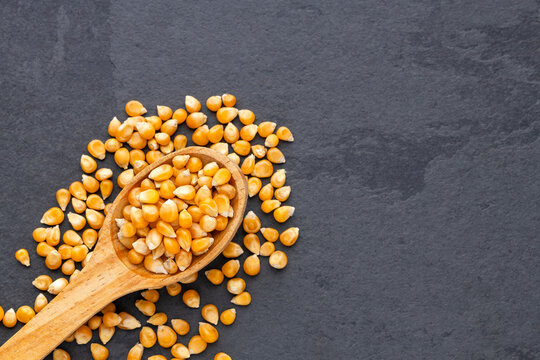 Popcorn kernels in a wooden spoon on a dark background, selective focus food photography