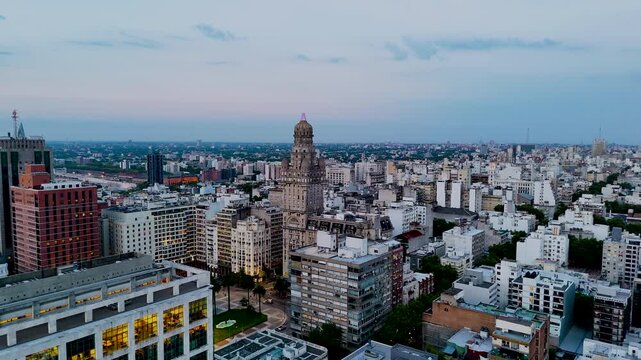 Drone view of Palacio Salvo and Plaza Independencia in central Montevideo at dusk, surrounded by historic and modern buildings with the city skyline extending into the distance.