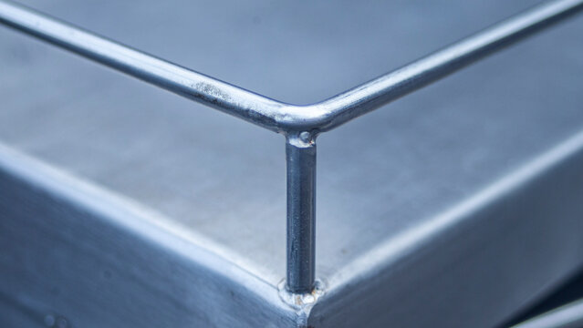 Close up of stainless steel railing weld joint on a metallic surface.A detailed close-up shot focusing on the weld joint corner of a stainless steel or iron protective railing. 