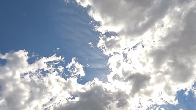 A pair of birds soar with their wings fully extended across a bright cloudy sky, gliding smoothly between gaps in the clouds overhead. This photo was taken outdoors during the day.