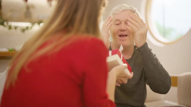 Family Christmas festive holiday celebration. Adult daughter giving gift to senior father at home. Happy Caucasian woman sharing special moment bonding with family and seasonal tradition celebrating