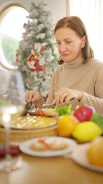 Senior parents and adult daughter enjoy Christmas dinner together at home. Happy family sharing festive holiday meal with roast chicken, salad and wine around dining table during seasonal celebration.