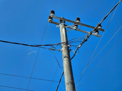 Concrete utility pole with electric power lines and insulators against a clear blue sky