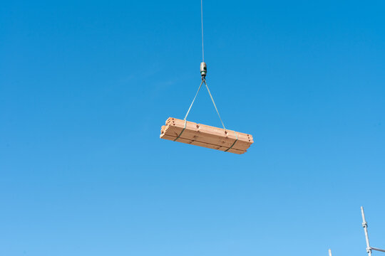 Wooden House Building Materials Lifted by Crane Against Blue Sky During House Framing Construction