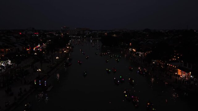 Boats adorned with colorful lanterns glide along the river in Hoi An, Vietnam, as night falls, reflecting lights on the water's surface