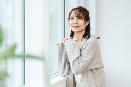 Woman in Her 40s or 50s Smiling Naturally by a Bright Window and Enjoying a Peaceful Moment