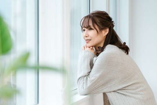 Woman in Her 40s or 50s Smiling Naturally by a Bright Window and Enjoying a Peaceful Moment