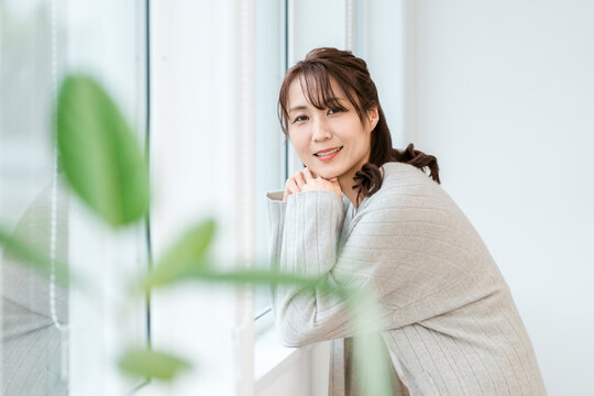 Woman in Her 40s or 50s Smiling Naturally by a Bright Window and Enjoying a Peaceful Moment