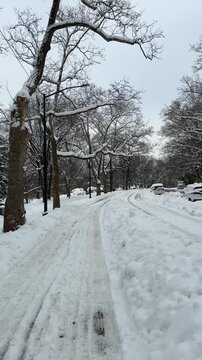 Vertical Video of green snow boots walking in snow in Central Park, camera pans up to see pencil Skyscrapers south of the park near Gapstow Bridge. 