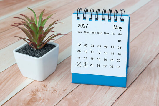 May 2027 desk calendar with potted plant on wooden desk.