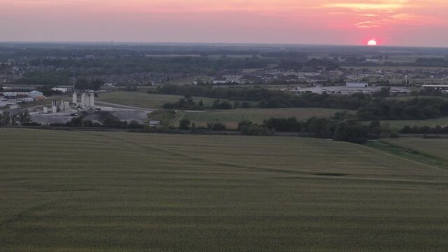 Aerial drone view vast Midwestern cornfield at sunset bordering suburban residential development and industrial infrastructure in Kansas