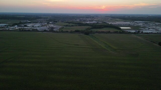 Aerial drone view vast Midwestern cornfield at sunset bordering suburban residential development and industrial infrastructure in Kansas