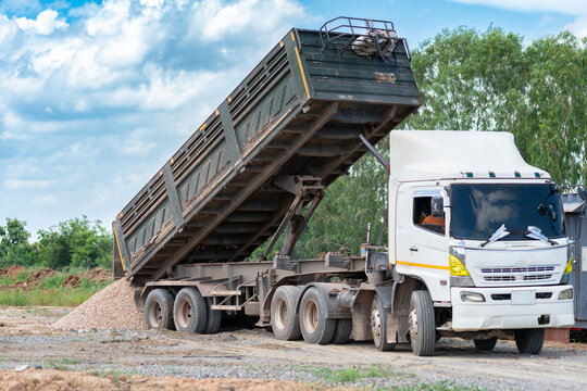 White heavy-duty dump semi-truck tipping its large trailer bed to unload gravel and soil at an outdoor construction site.