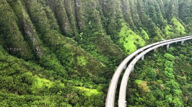 Aerial drone view of the H-3 highway disappearing into a tunnel under the steep green mountain wall, Oahu, United States