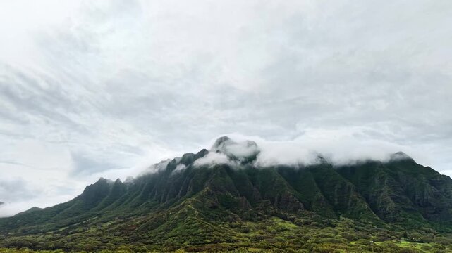 Aerial drone view of the fluted green cliffs of the Koolau Range with clouds hanging on the ridge, Oahu, United States