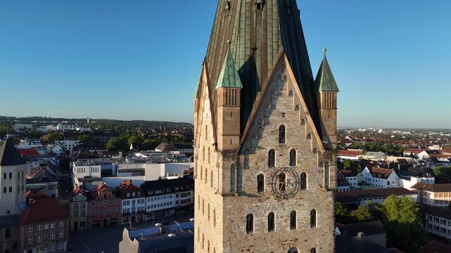 Vertical drone ascent climbs past the cathedral clock, roof structures and small turrets before tilting toward the twin crosses above.
