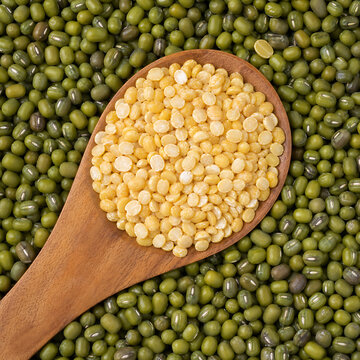 Top-down macro photo of split yellow moong dal on a wooden spoon over whole green mung beans background