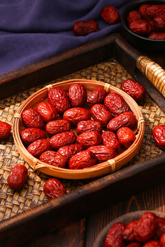 Dried red dates in a small bamboo basket on a wooden tray