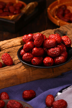 Fresh red jujube dates in a black bowl on rustic wooden board