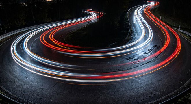 Long exposure light trails of traffic on a curved highway leading to the city skyline at night, Night traffic on a busy freeway with red and white blurred light streaks and cityscape.