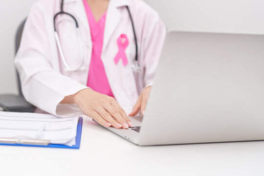 Professional doctor wearing lab coat using laptop and taking report notes on notebook for Breast Cancer Awareness month, World Cancer Day, National Cancer Survivors Month and Pink October in hospital