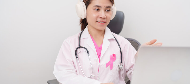 Professional doctor using laptop for telehealth, telemedical, online consultation and video meeting about Breast Cancer Awareness month, World Cancer Day and Pink October in hospital office concept