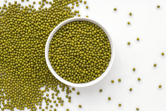 Top-down view of a ceramic bowl filled with organic dried green moong dal beans arranged on a clean white surface with scattered grains
