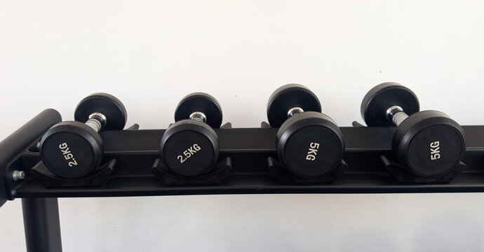 Black dumbbells of different weights arranged on a storage rack in a modern gym. Strength training and fitness equipment for weightlifting, functional workouts and exercise.