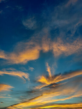 A beautiful vertical low-angle shot of a dynamic sunset sky filled with wispy golden-orange clouds contrasting against a deep blue evening sky.