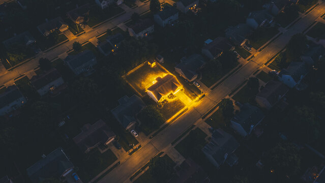 One house glows brightly in a dark suburban neighborhood at night