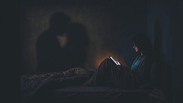 Woman on bed with tablet in dark room sees shadow of a loving couple
