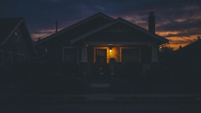 Two people sit on a home's porch illuminated by a warm light at dusk