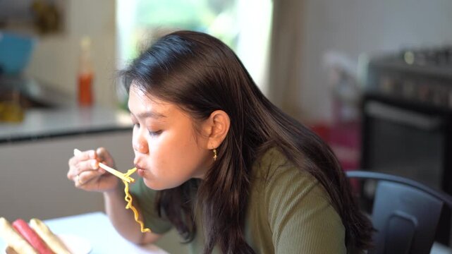 Asian woman eating instant noodles with chopsticks in the kitchen at home