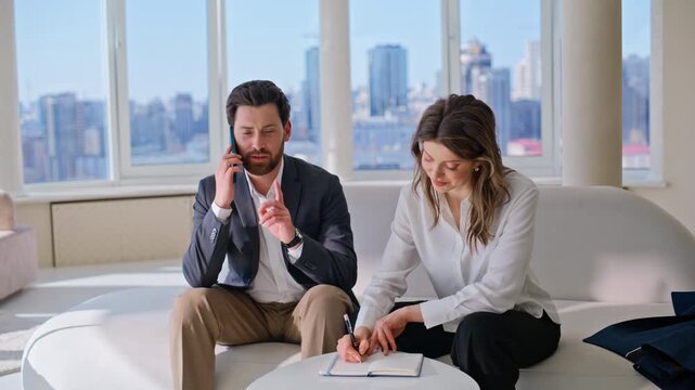 Colleagues discussing notes office lounge. Woman writing notebook man phone call