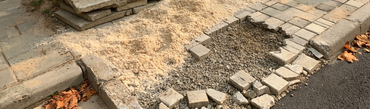 Paving Stone Repair in Progress: Broken paving stones on a pathway with sand and fallen leaves, indicating ongoing repair or construction work on an outdoor walkway.