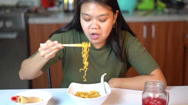 Young Asian woman eating instant noodles with chopsticks in the kitchen