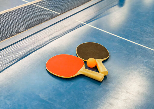  Table tennis paddles and ball on blue ping pong table near net
