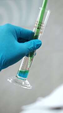 Close-up of laboratory technician measuring colored liquid with a graduated glass pipette and cylinder during precise scientific analysis and laboratory testing.