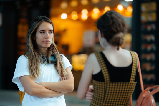 Upset Offended Woman Standing With Arms Crossed Looking At Friend. Annoyed girlfriend glares unhappily toward another girl during a tense urban conversation