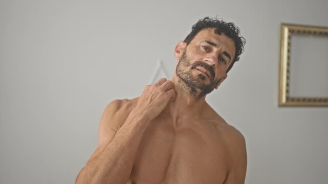 Shirtless man rubs his neck and collarbone while massaging tense muscles in a minimalist studio setting; introspection recovery.
