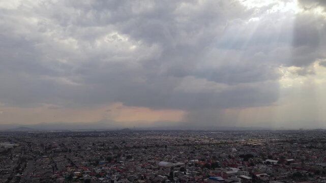 Smooth frontal aerial drone view over residential neighborhoods in Ecatepec, Mexico, with cloudy skies, sun rays and urban streets during daylight