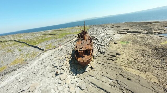 FPV camera banks and tilts along the rusted Plassey hull stranded on rocky coastal flats beside the open Atlantic.
