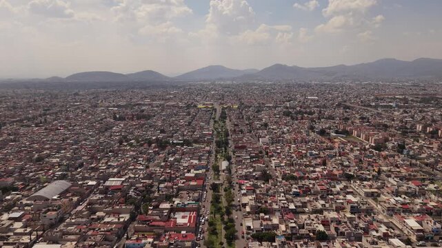 Aerial drone view over a divided two-way avenue in Ecatepec, Mexico, with moving traffic, pedestrians and urban neighborhoods during a sunny day