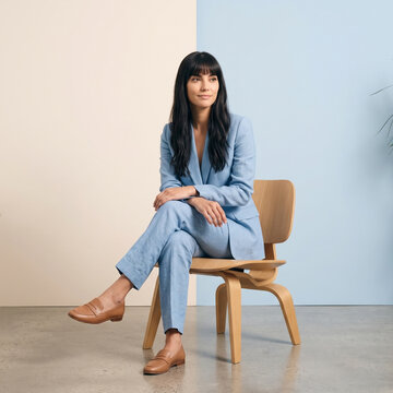Full body portrait of stylish woman sitting on wooden chair wearing blue suit and leather loafers