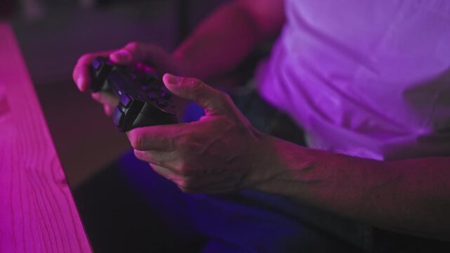 Man holding game controller with thumbs on joystick and visible hands, seated in studio under purple lighting; concentration immersion.