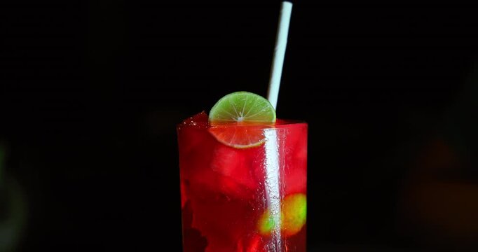 Fresh red cocktail with lime slice and drinking straw served in tall glass in luxury bar. Chilled alcoholic aperitif drink at night club. Holiday party vacation concept.