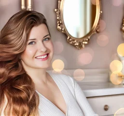 Woman smiling, showcasing her long, healthy hair and radiant beauty in an elegant setting with a blurred mirror and bokeh lights © Studio ANNA