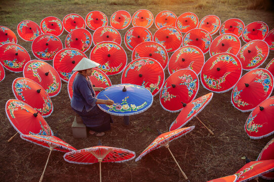 Authentic Thai heritage brought to life. A skilled Chiang Mai woman artisan creates intricate art on a traditional umbrella. An ideal visual for tourism, travel banners, and cultural stories.